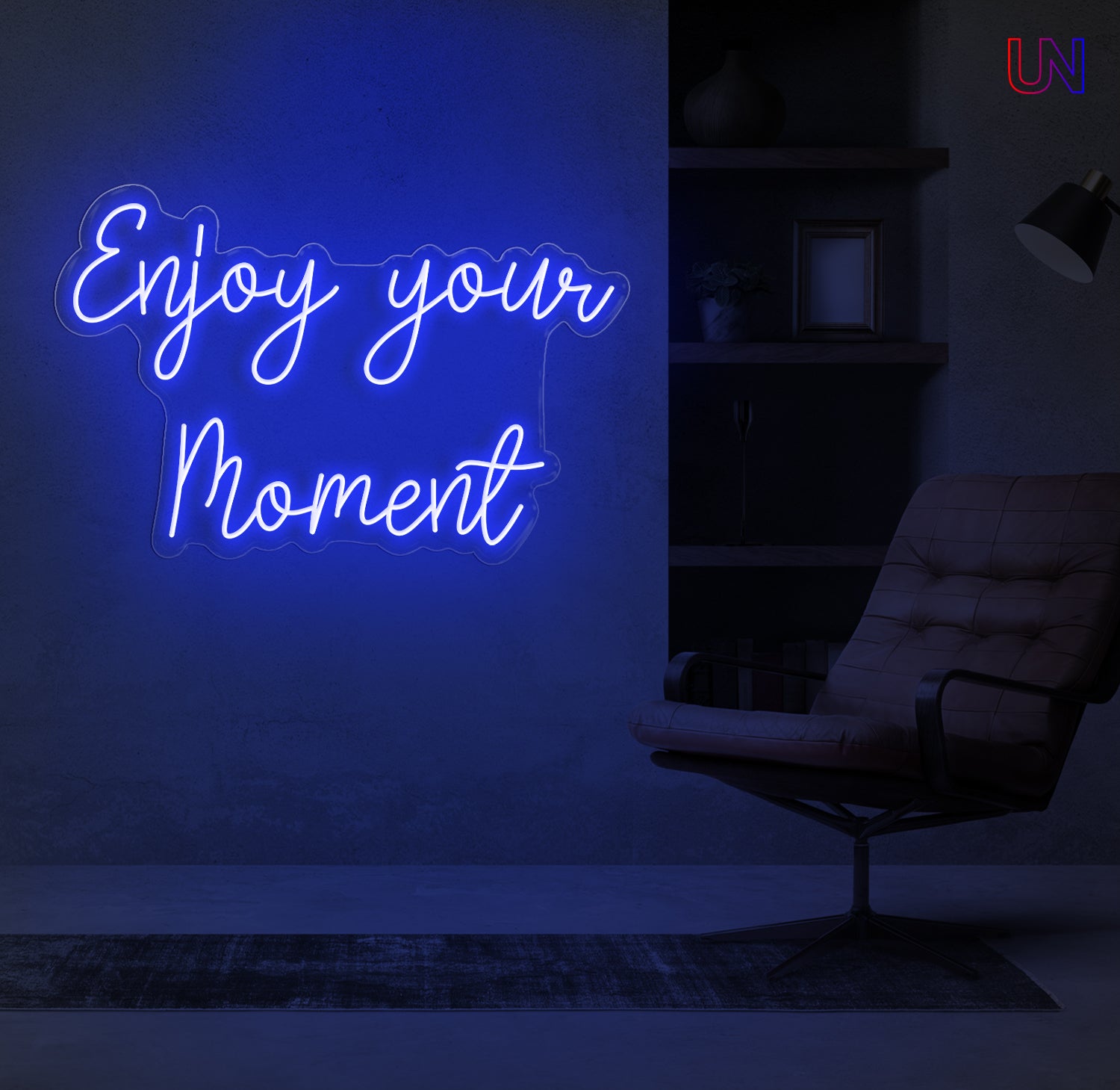 Neon sign with the words “Enjoy Your Moment” glowing above a modern chair in a cozy reading corner