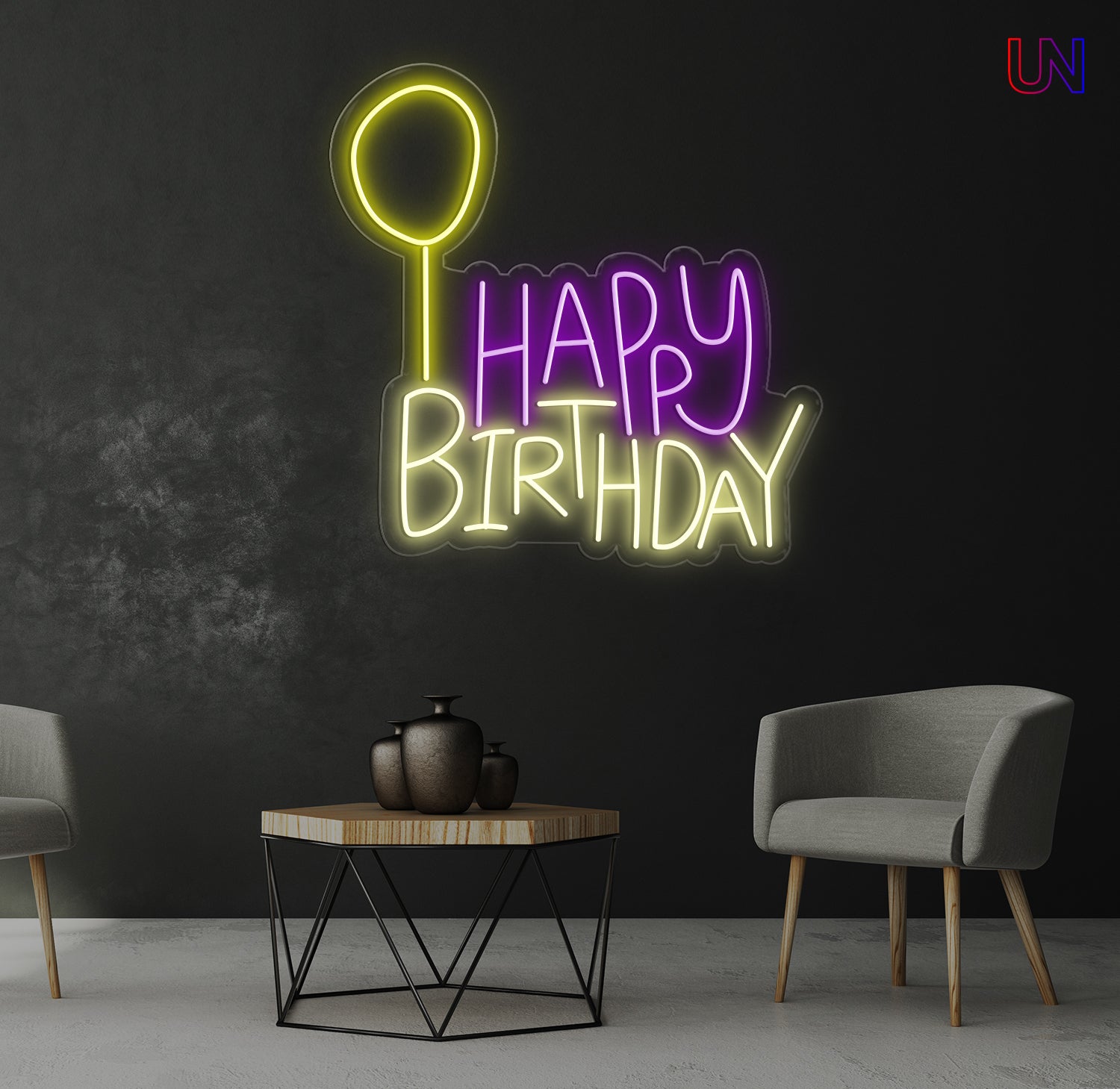 Neon 'Happy Birthday' sign on a dark wall with two chairs and a table in the foreground.