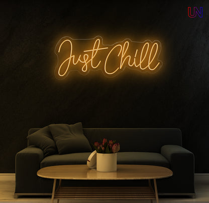 Neon sign reading 'Just Chill' above a dark sofa in a dimly lit room.