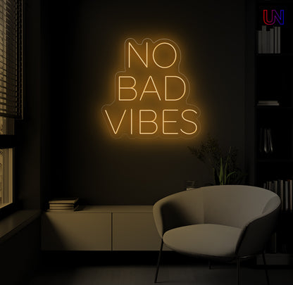 Neon sign with 'No Bad Vibes' in a dark room with a chair and books.