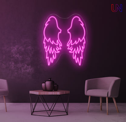 Neon pink angel wings light fixture on a dark purple wall with a table and chairs in the foreground.
