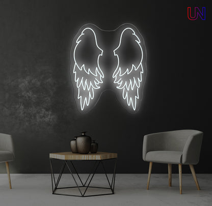 Neon angel wings light fixture on a dark wall with two chairs and a table in the foreground.
