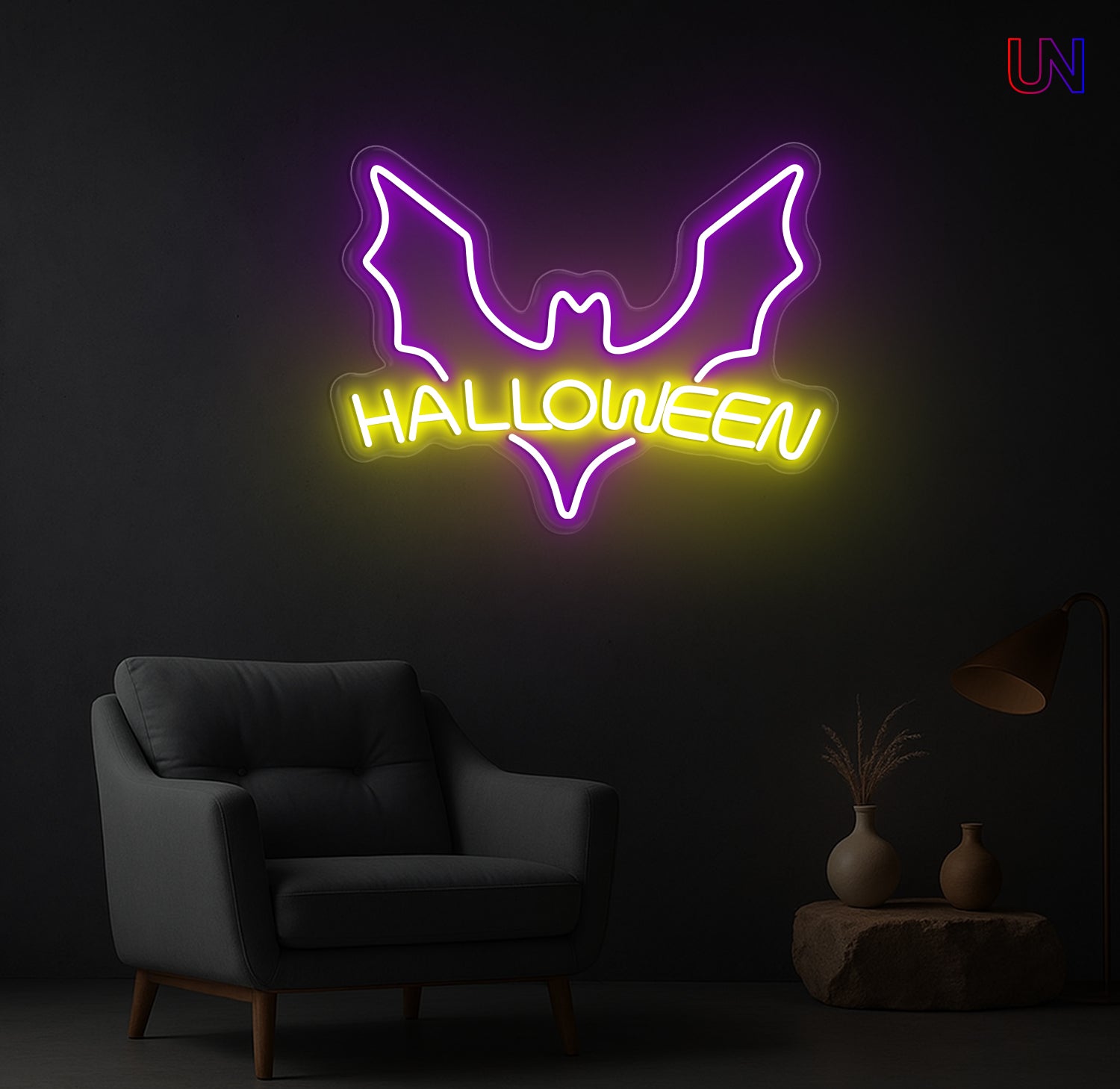A vibrant purple bat silhouette with glowing yellow "HALLOWEEN" text underneath, illuminated as an LED neon sign on a dark wall above a grey armchair and a small table with vases.